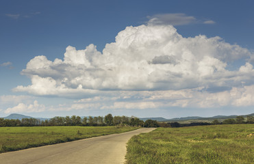 Summer countryside landscape with stormy cumulonimbus clouds in the sky and empty road crossing the grasslands of the Transylvania region, Romania.
