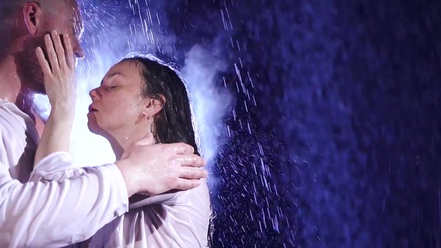 Couple in white clothes in the rain and moonlight are and gently caress each other