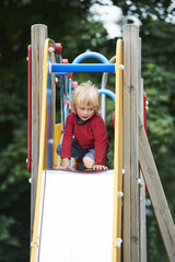 Fototapeta na wymiar Little child blond boy sliding down a slide at the summer playground