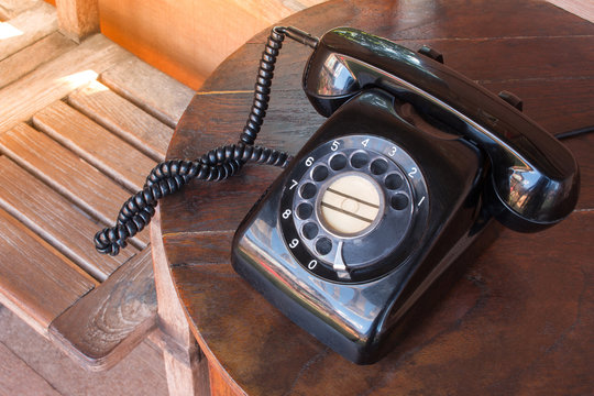 Old black phone with dust, circle dialpad and scratches on wooden retro desk. Vintage desk telephone concept.