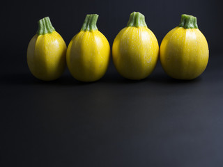 Round yellow zucchini squash lit from the side, isolated on black background