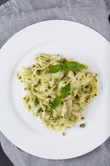 Still life - Homemade pasta from basil and arugula with green pesto in a white plate on a dark background.