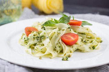 Homemade pasta from basil and arugula with green pesto in a white plate on a dark background. Italian Cuisine