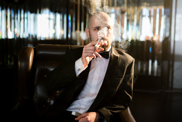 A brutal man in a dress coat smokes a cigar.