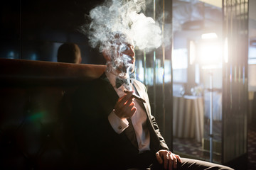 A brutal man in a dress coat smokes a cigar.