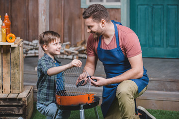 side view of smiling father and son preparing grill for barbecue