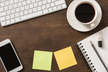 Close-up view of smartphone with blank screen, keyboard, blank notes and cup of coffee at workplace, small office concept