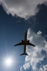 Airplane silhouette in the sky with sun and clouds around.