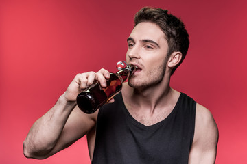 Handsome young man in black vest drinking beer and looking away