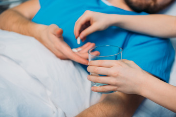 son giving pills and glass of water to his sick father laying at ward, dad and son