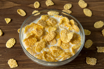 Corn flakes in a glass bowl with milk on a wooden surface
