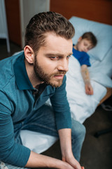 Obraz premium portret zamyślonego taty siedzącego obok chorego syna w szpitalnym łóżku