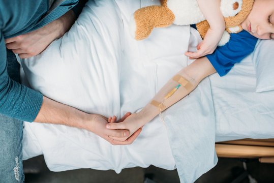 Overhead View Of Little Boy With Drop Counter Sleeping In Hospital Bed With Father Near By