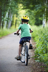 Naklejka premium Child boy on a bicycle on bicycle path in summer. Boy cycling outdoors in safety helmet