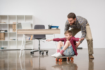 Businessman freelancer having fun with son on skateboard at home office