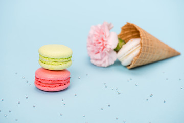 Group of handmade macarons in waffle cone and pink flower on blue surface. macarons background concept