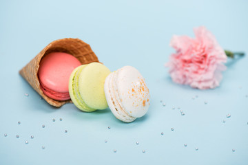 Group of handmade macarons in waffle cone and pink flower on blue surface. macarons background concept