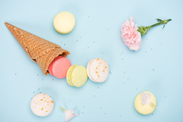 Top view of sweet macarons in waffle cone with pink Carnation. Colorful sweets background
