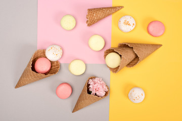 Top view of fresh homemade macarons, waffle cones and Carnation flower on colorful surface. Sweet macarons pattern concept