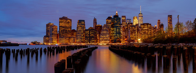 New York City Manhattan skyline with skyscrapers over Hudson River illuminated lights at dusk after sunset.