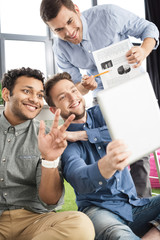 Smiling young businessmen using digital tablet and showing charts, business teamwork concept