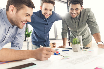 Three young businessmen leaning at table and working at project together, business teamwork concept