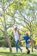 Fototapeta premium Mother and son walking in the park with football
