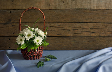 Fototapeta na wymiar Beautiful white flowers in the flower basket and green leaf on light violet cloth in dim light room