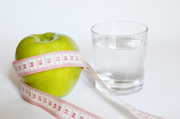 Measuring tape around wrapped green apple and a glass of water