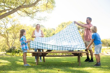Family spreading the tablecloth on picnic table