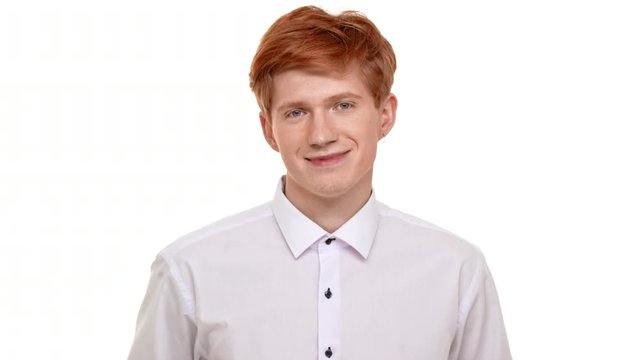 Handsome young calm redhead Caucasian man calmly standing on white background and smiling at camera