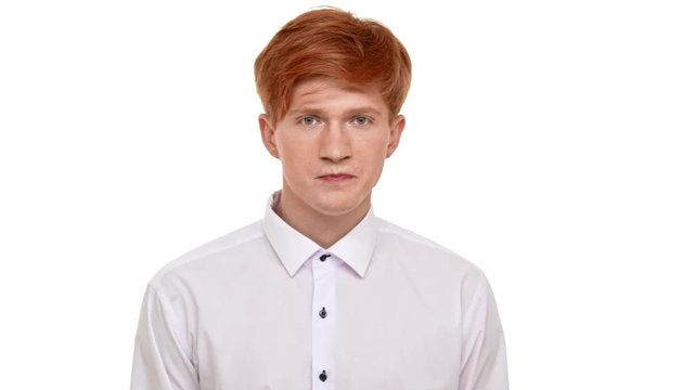 Severe handsome redhead Caucasian young man heavily breathing and looking at camera with rage. Footage on white background in slowmotion