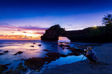 professional photographer with camera and tripod in Tanah Lot Temple at sunset, Bali in Indonesia.(Dark)Seascape.