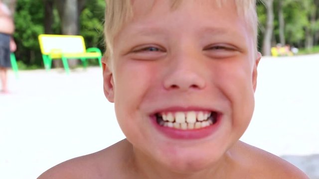 Closeup portrait of cute funny cheerful boy making silly faces into camera at sunny sandy beach. Real time full hd video footage.
