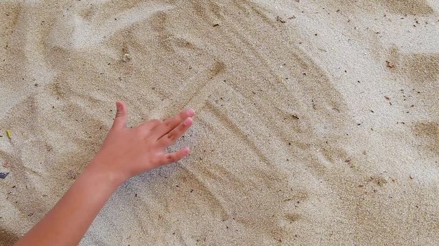 Closeup of little child hand drawing small house and heart shape with his fingers in sandy beach background. Real time full hd video footage.