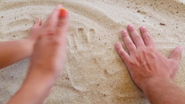 Closeup of tanned human hands of family of three persons. Father, mother and little son making handprints in white sand on river beach. Togetherness concept. Real time full hd video footage.