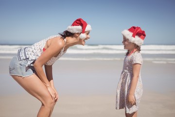 Cheerful woman with daughter wearing Santa hat at beach