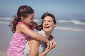 Happy mother piggybacking daughter at beach