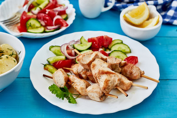 Grilled chicken kebabs and fresh vegetable salad,young potatoes on a blue wooden background.horizontal