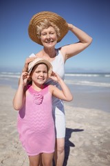 Portrait of girl with grandmother wearing sun hat at beach