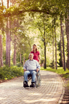 daughter in the park pushing enjoying senior man in wheelchair.