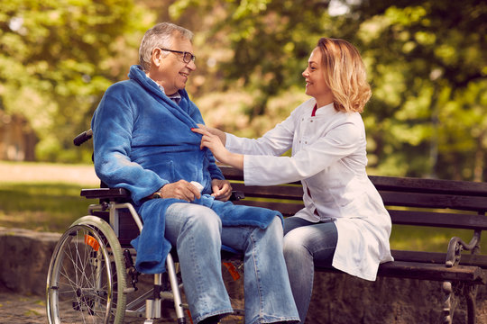 Caregiver nurse helping disabled senior patient in wheelchair.