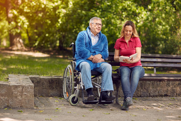 Disabled man in park spending time together with his daughter reading book.