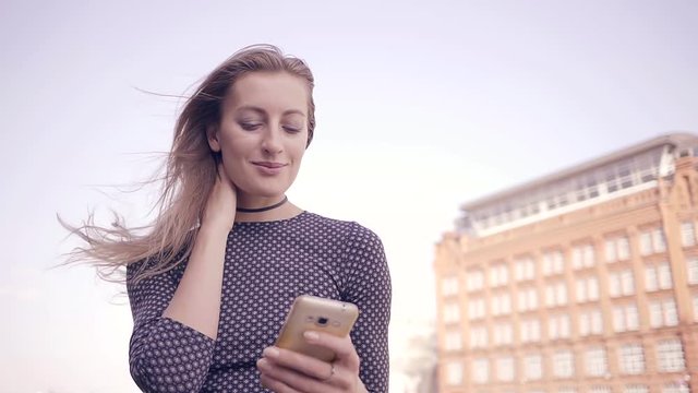 Pretty young girl talking on the Internet with the help of cell phone walking in the city