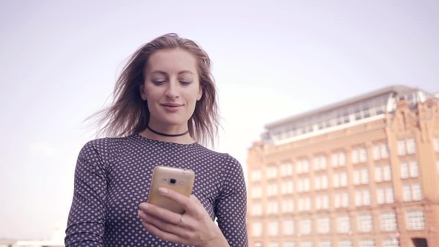 Pretty young girl talking on the Internet with the help of cell phone walking in the city