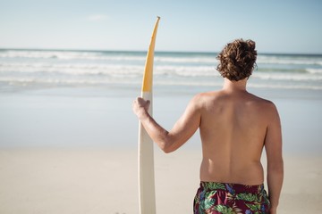 Rear view of shirtless man holding surfboard at beach