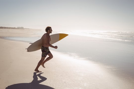 Shirtless man running while holding surfboard at beach