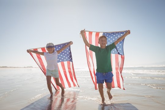 Siblings holding American flags while running at beach
