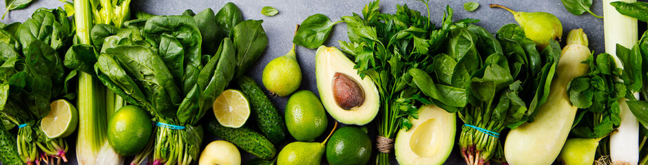 Green vegetables and herbs assortment on a grey stone background. Top view.