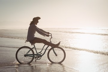 Fototapeta na wymiar Side view of cheerful woman riding bicycle on shore at beach